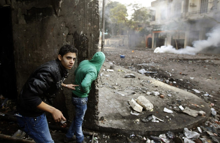 Hai thanh niên biểu tình nấp sau bức tường khi cảnh sát chống bạo động ném lựu đạn cay giải tán đám đông. Hai thanh niên biểu tình nấp sau bức tường khi cảnh sát chống bạo động ném lựu đạn cay giải tán đám đông.