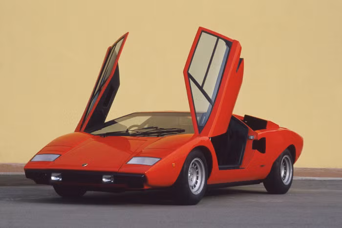 2. Lamborghini Countach (1974 - 1990) Countach là mẫu xe thể thao động cơ đặt giữa được Lamborghini đưa vào sản xuất trong khoảng thời gian từ năm 1974 đến 1990. Đây có thể xem là mẫu xe tiên phong và định hình phong cách hầm hố, góc cạnh của các dòng xe Lamborghini nói riêng và siêu xe nói chung. Thiết kế đẩy cabin lái về phía trước nhằm tăng diện tích cho động cơ, và đặc biệt là cửa ra vào đóng mở kiểu cắt kéo cũng từ chính Countach mà ra. Cái tên Countach bản thân nó cũng có một "tiểu sử" thú vị riêng. Đây là một từ cảm thán trong ngôn ngữ địa phương tại Ý có tên Piedmontese, thường được sử dụng bởi nam giới mỗi khi nhìn thấy một người phụ nữ tuyệt đẹp. Những lô Countach đầu tiên sử dụng chung động cơ V12 4 lít của Miura, sau này được nâng cấp lần lượt lên 5 lít rồi 5,2 lít. Có cả thảy 5 phiên bản Countach được sản xuất, bao gồm LP400, LP400S, LP500S, LP5000QV và một phiên bản đặc biệt nhân kỷ niệm 25 năm Countach ra đời. Tổng cộng, Lamborghini đã chế tạo được 2.042 chiếc Countach trong vòng đời 16 năm của nó. Cái tên Countach chỉ bị lu mờ phần nào kể từ khi kẻ kế nhiệm nó xuất hiện, Lamborghini Diablo.