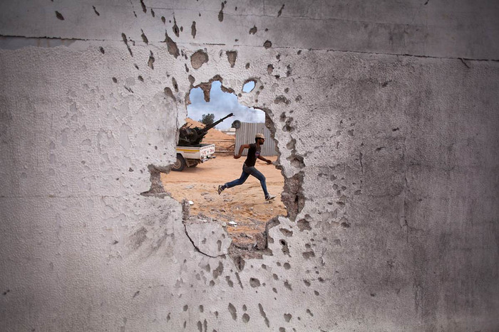 Ảnh chụp một binh sỹ nổi dậy chạy vụt qua lỗ thủng bị đạn bắn ở Sirte, Libya. Ảnh chụp một binh sỹ nổi dậy chạy vụt qua lỗ thủng bị đạn bắn ở Sirte, Libya.