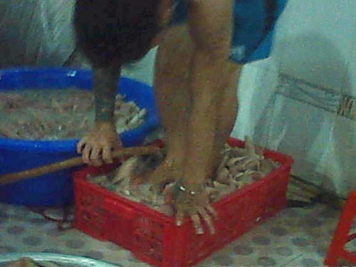 Lấy chân đạp lên da heo đã luộc chín đựng trong thau để tẩy sạch da - Ảnh: Hải Nguyên