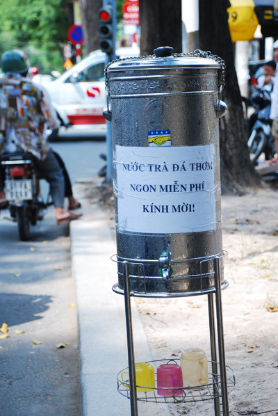 Người nấu trà đá còn trân trong kính mời người đi đường. Ảnh Báo TNO Người nấu trà đá còn trân trong kính mời người đi đường. Ảnh Báo TNO