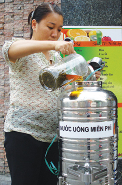 Một chủ nhân của thùng trà miễn phí đổ thêm trà vào bình cho khách qua đường. Ảnh TNO Một chủ nhân của thùng trà miễn phí đổ thêm trà vào bình cho khách qua đường. Ảnh TNO