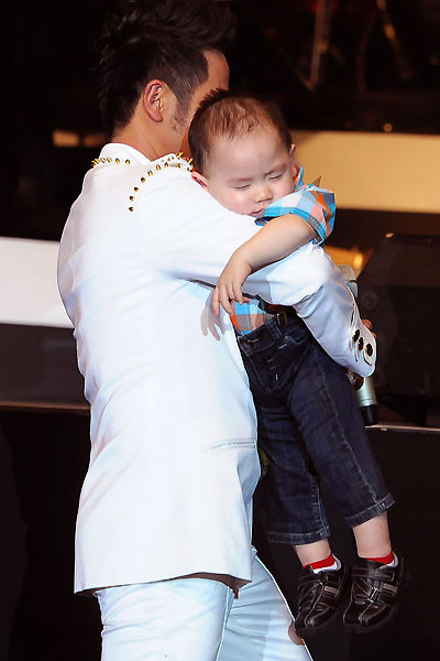 Bằng Kiều bế cậu con trai út trên tay. Vì trời đã khuya nên cậu bé ngủ ngon lành.