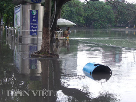 Dưới có hồ, còn phía trên lòng đường, vỉa hè cũng lại thành ao sau mưa Nước không thoát kịp xuống cống, ùn ùn đùn nước lên và chảy tràn xuống hồ Gươm Người đàn ông này bị mắc kẹt trên vỉa hè Nước lênh láng cả một đoạn dài phía đường Đinh Tiên Hoàng Có những chỗ ngập sâu đến nửa mét Bãi để xe ô tô ven hồ Gươm cũng bị ngập khá sâu Nước cống hòa nước mưa, ứ đọng, đen ngòm và kèm theo đó là mùi hôi thối nồng nặc Từng mảng váng bẩn cuộn lại theo dòng nước xoáy tràn xuống hồ Gươm Nước bẩn ào ào xối xuống lòng hồ