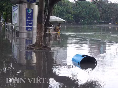 Dưới có hồ, còn phía trên lòng đường, vỉa hè cũng lại thành ao sau mưa Nước không thoát kịp xuống cống, ùn ùn đùn nước lên và chảy tràn xuống hồ Gươm Người đàn ông này bị mắc kẹt trên vỉa hè Nước lênh láng cả một đoạn dài phía đường Đinh Tiên Hoàng Có những chỗ ngập sâu đến nửa mét Bãi để xe ô tô ven hồ Gươm cũng bị ngập khá sâu Nước cống hòa nước mưa, ứ đọng, đen ngòm và kèm theo đó là mùi hôi thối nồng nặc Từng mảng váng bẩn cuộn lại theo dòng nước xoáy tràn xuống hồ Gươm Nước bẩn ào ào xối xuống lòng hồ
