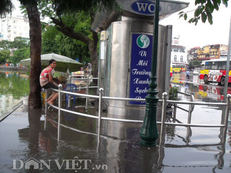 Sợ lội nước bẩn, người phụ nữ này phải ngồi co trên thành rào chắn chờ nước rút