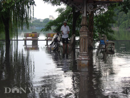 Dưới có hồ, còn phía trên lòng đường, vỉa hè cũng lại thành ao sau mưa Nước không thoát kịp xuống cống, ùn ùn đùn nước lên và chảy tràn xuống hồ Gươm Người đàn ông này bị mắc kẹt trên vỉa hè Nước lênh láng cả một đoạn dài phía đường Đinh Tiên Hoàng Có những chỗ ngập sâu đến nửa mét Bãi để xe ô tô ven hồ Gươm cũng bị ngập khá sâu Nước cống hòa nước mưa, ứ đọng, đen ngòm và kèm theo đó là mùi hôi thối nồng nặc Từng mảng váng bẩn cuộn lại theo dòng nước xoáy tràn xuống hồ Gươm Nước bẩn ào ào xối xuống lòng hồ