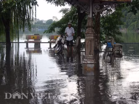 Dưới có hồ, còn phía trên lòng đường, vỉa hè cũng lại thành ao sau mưa Nước không thoát kịp xuống cống, ùn ùn đùn nước lên và chảy tràn xuống hồ Gươm Người đàn ông này bị mắc kẹt trên vỉa hè Nước lênh láng cả một đoạn dài phía đường Đinh Tiên Hoàng Có những chỗ ngập sâu đến nửa mét Bãi để xe ô tô ven hồ Gươm cũng bị ngập khá sâu Nước cống hòa nước mưa, ứ đọng, đen ngòm và kèm theo đó là mùi hôi thối nồng nặc Từng mảng váng bẩn cuộn lại theo dòng nước xoáy tràn xuống hồ Gươm Nước bẩn ào ào xối xuống lòng hồ