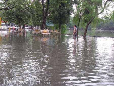 Dưới có hồ, còn phía trên lòng đường, vỉa hè cũng lại thành ao sau mưa Nước không thoát kịp xuống cống, ùn ùn đùn nước lên và chảy tràn xuống hồ Gươm Người đàn ông này bị mắc kẹt trên vỉa hè Nước lênh láng cả một đoạn dài phía đường Đinh Tiên Hoàng Có những chỗ ngập sâu đến nửa mét Bãi để xe ô tô ven hồ Gươm cũng bị ngập khá sâu Nước cống hòa nước mưa, ứ đọng, đen ngòm và kèm theo đó là mùi hôi thối nồng nặc Từng mảng váng bẩn cuộn lại theo dòng nước xoáy tràn xuống hồ Gươm Nước bẩn ào ào xối xuống lòng hồ