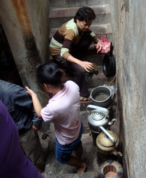 Một phụ nữ luộc trứng và một cô gái đang nấu nước bằng bếp than tổ ong ngay khoảng không gian dẫn lên cầu thang trên gác hai (ảnh chụp tại ngõ 44 Hàng Buồm) - Ảnh: My Lăng.