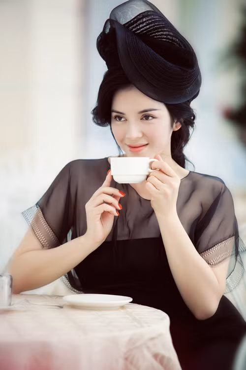 Chiếc mũ đen có chất liệu dày dặn, tạo khối hình hoa cách điệu hòa quyện cùng chiếc đầm đen có điểm nhấn phần trên bằng cách đổi chất liệu vải sheer bên trên và lụa bên dưới tạo ra những khối màu đen đồng nhất mà vẫn khác biệt về sắc độ.