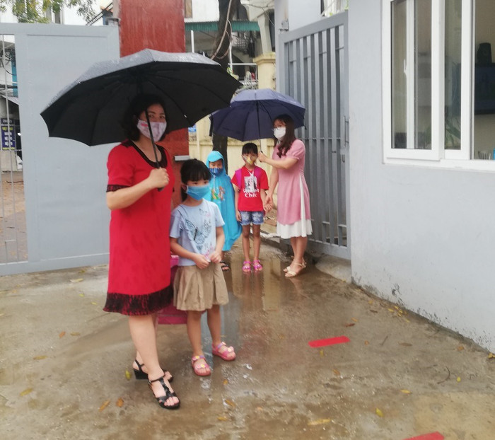Học sinh ngày thứ hai đến trường trời mưa to được các cô giáo ra cổng đón vào lớp kiểm tra y tế, thân nhiệt. Ảnh: NVCC.
