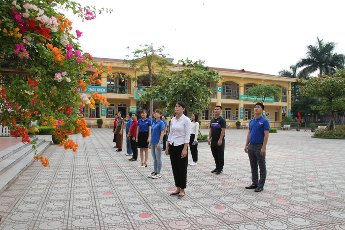 Ban giám hiệu, cán bộ, giáo viên, nhân viên nhà trường thực hiện nghi thức làm lễ chào cờ. Ảnh: Vũ Phương