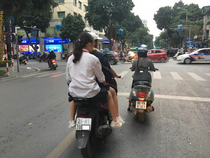 Phụ huynh kẹp hai học sinh đầu trần không nón mũ bảo hiểm băng băng trên đường. Ảnh: Vũ Phương. Phụ huynh kẹp hai học sinh đầu trần không nón mũ bảo hiểm băng băng trên đường. Ảnh: Vũ Phương.