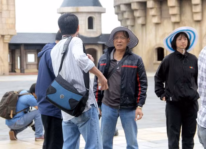 Đạo diễn Lại Văn Sâm đội mũ rộng vành, mặc áo khoác trao đổi công việc với đồng nghiệp.