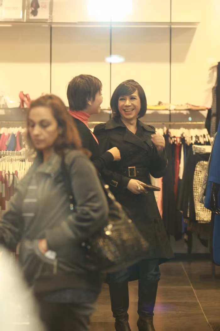 Long Nhật đội tóc giả và trang điểm khá đậm, anh đi bốt, mặc áo măng tô đen dài trông thanh thoát và đầy nữ tính