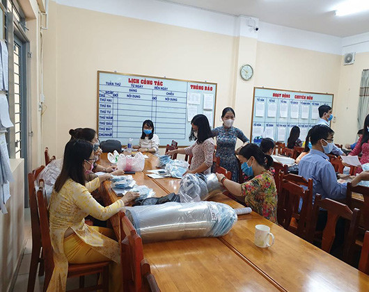 Giáo viên chủ nhiệm phân loại khẩu trang, nón chống giọt bắn cho học sinh trước khi vào lớp (ảnh: P.L)