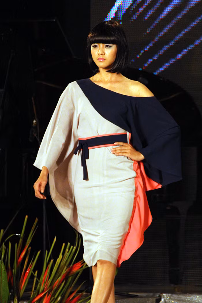 Chiếc đầm liền lệch vai cá tính này dành cho những cô nàng có thân hình bốc lửa và khuôn mặt góc cạnh một chút. Nét chấm phá độc đáo của chiếc váy là hai dải bèo mềm mại hai bên thân váy. Chính kiểu tóc ngắn mái ngang trẻ trung của người mẫu làm cho chúng ta gợi nhớ đến chiếc áo Kimono của dân tộc Nhật Bản.