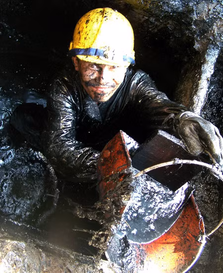 Suốt ngày tiếp xúc với bùn dơ, nhưng lương của người công nhân móc cống quá thấp so với giám đốc - Ảnh: T.TRUNG (Tuổi Trẻ)