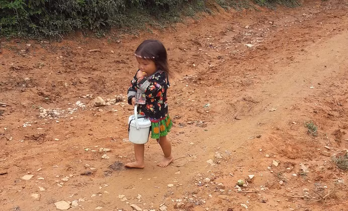 Em bé học sinh vừa đi bộ vừa bốc cơm để ăn.