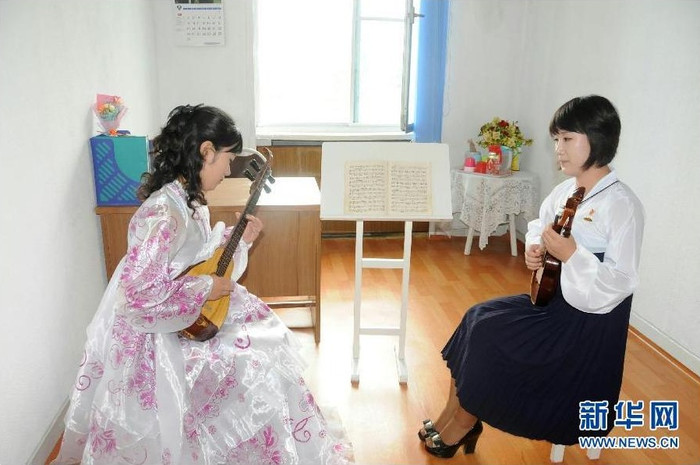 Một giáo viên trong trang phục truyền thống đang dạy học sinh chơi đàn dân gian.