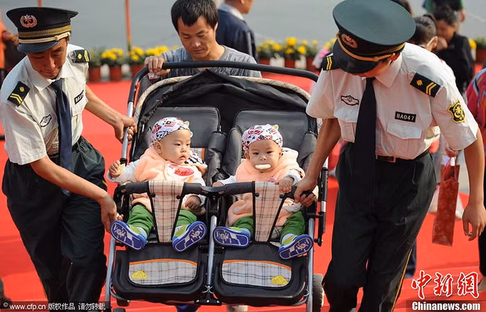 Các nhân viên an ninh giúp một người bố đưa hai em bé lên bậc thang.