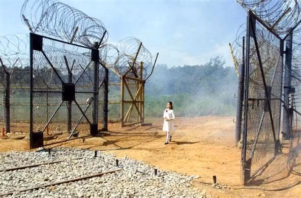 Trên tay cầm một bông hoa, bé gái đi qua cánh cổng dẫn vào khu phi quân sự.