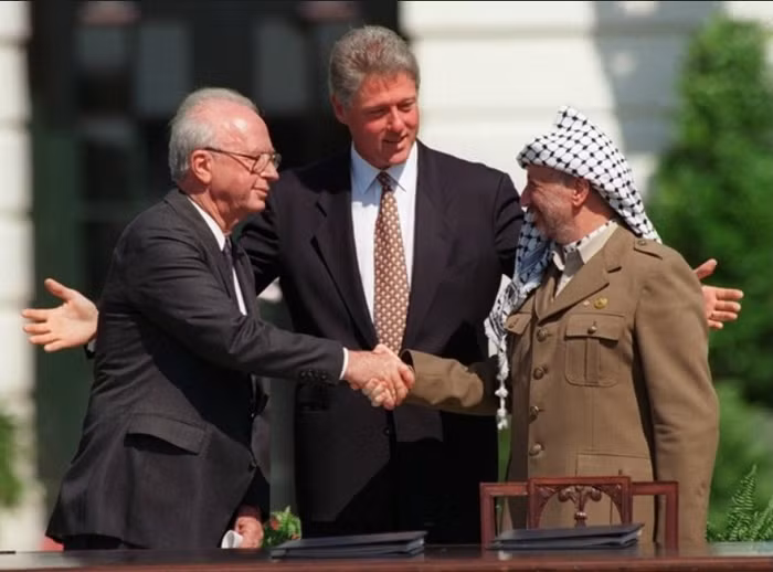 Thủ tướng Israel - Yitzhak Rabin (trái) và Yasser Arafat, nhà lãnh đạo của Tổ chức Giải phóng Palestine, bắt tay trước một đám đông trên bãi cỏ Nhà Trắng vào ngày 13/9/1993. Đây là cái bắt tay đầu tiên trước công chúng của hai nhà lãnh đạo trong các cuộc đàm phán hòa bình giữa Israel và các vùng lãnh thổ Palestine. Mặc dù tương đối lạc quan, thỏa thuận đã không bao giờ trở thành hiện thực.