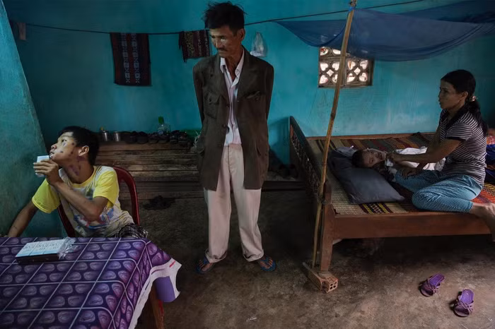 Ông Le Van Dan, một cựu chiến binh, mặc chiếc áo bộ đội đã cũ sờn nhìn hai người cháu trai của mình trong căn phòng cũ kĩ. Hai cháu của ông bị khuyết tật từ lúc sinh ra do ảnh hưởng của chất độc da cam mà ông đã nhiễm phải.