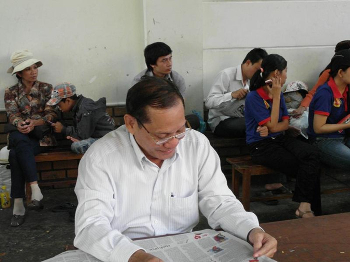 Ông Trương Quốc Thắng nhàn nhã đọc báo, chờ con thi. Ảnh chụp trước điểm thi trường CĐ Viễn Đông, Ảnh: Dương Cầm