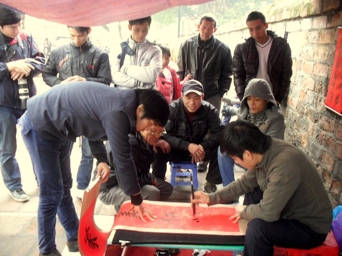 "Ông đồ" trẻ này đang viết một vế câu đối đỏ, nhiều bạn trẻ khác đứng xem. "Ông đồ" trẻ này đang viết một vế câu đối đỏ, nhiều bạn trẻ khác đứng xem.