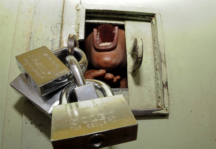 Một người biểu tình Uganda đang cố tìm chỗ thở sau khi bị cảnh sát chống bạo động bắt và xịt hơi cay vào quầy hàng bị khoá trái Một người biểu tình Uganda đang cố tìm chỗ thở sau khi bị cảnh sát chống bạo động bắt và xịt hơi cay vào quầy hàng bị khoá trái