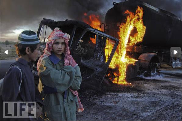 Hai học sinh đứng gần chiếc xe tải chờ nhiên liệu của NATO cháy đen sau cuộc tấn công của các tay súng tại tỉnh Baluchistan, Pakistan.