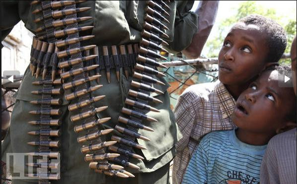 Những đứa trẻ đang nhìn chằm chằm vào một người lính trang bị đầy súng đạn đi tuần tra tại Burgabo, Somalia.