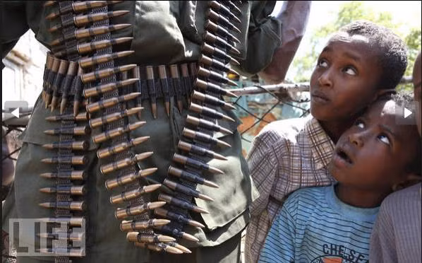 Những đứa trẻ đang nhìn chằm chằm vào một người lính trang bị đầy súng đạn đi tuần tra tại Burgabo, Somalia.