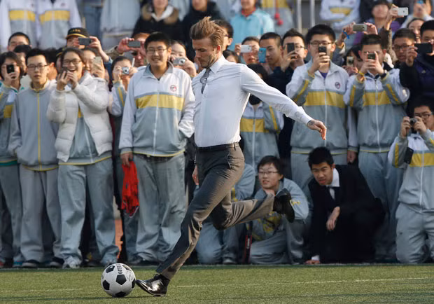 Trong bộ quần bó và áo chật, Becks có thể trình diễn các kỹ năng chơi bóng trước các em học sinh tại Bắc Kinh..