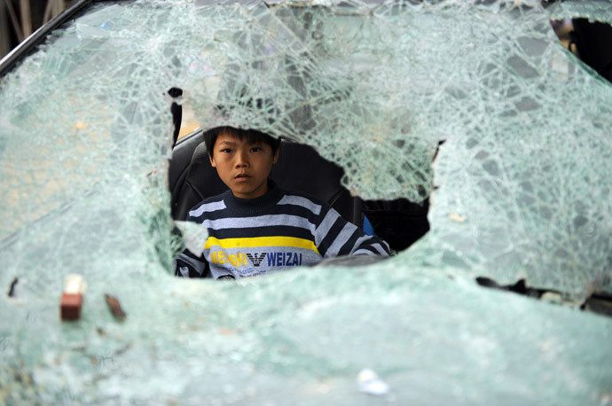 Một cậu bé ngồi bên trong chiếc xe hơi bị đập vỡ kính trước trong cuộc đụng độ hồi tuần trước.