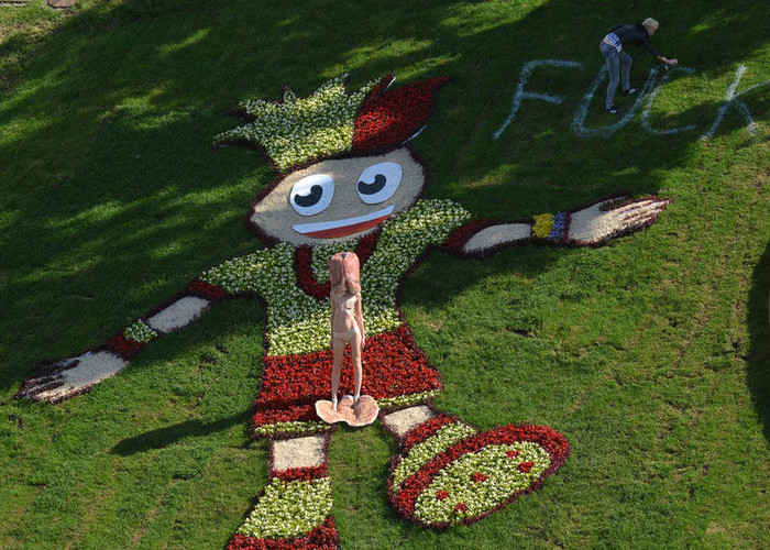 Một người đẹp thuộc nhóm FEMEN ngực trần đứng biểu tình trước linh vật EURO 2012, trong khi, thành viên còn lại xịt thông điệp biểu tình lên cỏ trong công viên ở Ukraine