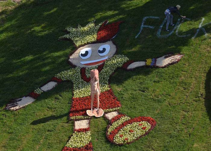 Một người đẹp thuộc nhóm FEMEN ngực trần đứng biểu tình trước linh vật EURO 2012, trong khi, thành viên còn lại xịt thông điệp biểu tình lên cỏ trong công viên ở Ukraine