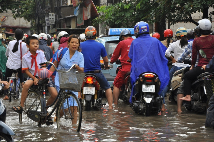Nước ngập cao nên đi xe đạp khó khăn, một phụ huynh phải xuống dắt xe trong khi con vẫn ngồi ở trên cho khỏi ướt Nước ngập cao nên đi xe đạp khó khăn, một phụ huynh phải xuống dắt xe trong khi con vẫn ngồi ở trên cho khỏi ướt