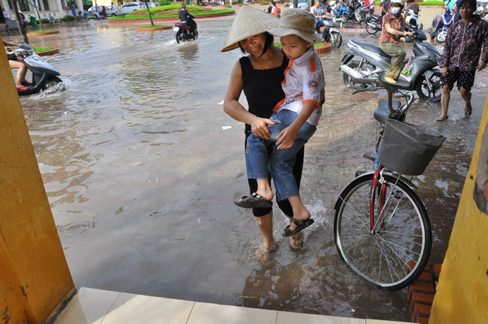 Để con không bị ướt quần áo, một phụ huynh bế con đi qua nơi ngập nước đến lối đi cao hơn Để con không bị ướt quần áo, một phụ huynh bế con đi qua nơi ngập nước đến lối đi cao hơn
