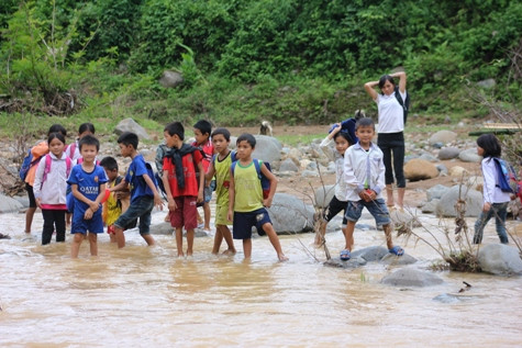 Mỗi khi tan trường, hàng chục học sinh tập hợp lại thành từng nhóm, lội lõm bõm ven bờ đến vị trí đặt cầu tạm để qua suối. Ảnh: Xuân Quang.