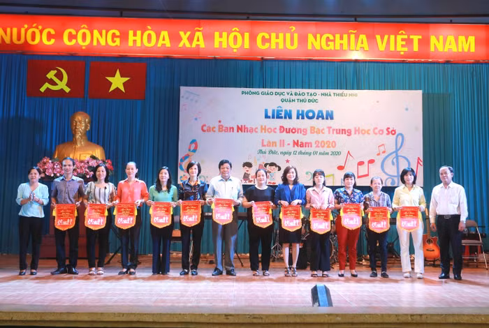 Thầy Dương Hoàng Tuấn (Trưởng phòng Giáo dục và Đào tạo) và chị Lê Thị Hiếu (Phó giám đốc Nhà thiếu nhi) tặng cờ lưu niệm cho đại diện Ban giám hiệu và giáo viên phụ trách của các trường trung học cơ sở. Ảnh: Cẩm Vân.