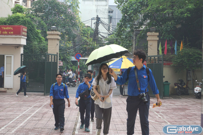 Tình nguyện viên che ô cho thí sinh tại Điểm thi Trường Trung học phổ thông Kim Liên. (Ảnh: Đào Hiền) GDVN 2.JPG
