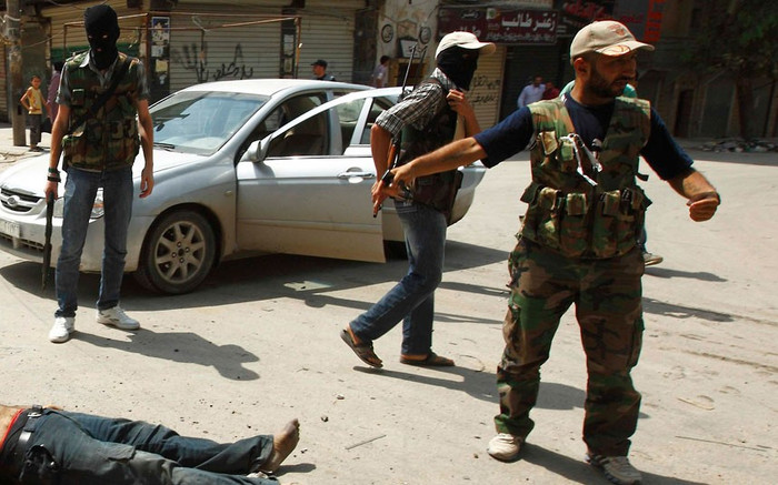 Một thành viên của Quân đội Syria Tự do chỉ vào thi thể của người đàn ông mà họ cho rằng thuộc nhóm dân quân Shabiha ủng hộ Tổng thống Bashar al-Assad.