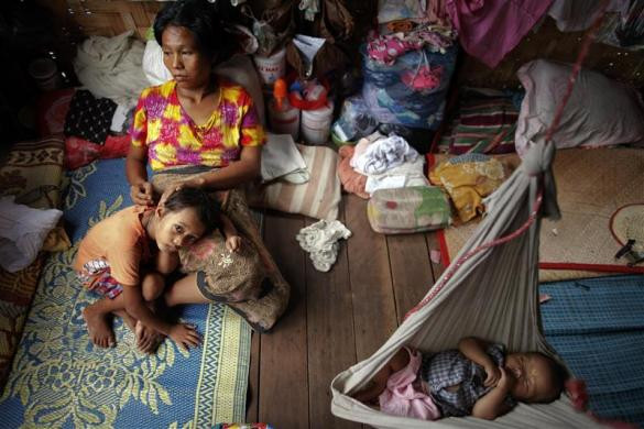 Ma Mon, bệnh nhân HIV, nắm tay cô con gái 5 tuổi Myat Noe trong khi con trai Ei Ei Phyu đang ngủ trên võng. Cả 2 đứa con của cô đều được chẩn đoán nhiễm HIV dương tính.