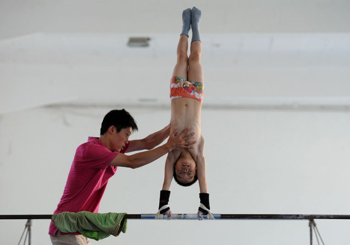 Huấn luyện viên giúp một cậu bé đội thể dục dụng cụ trong quá trình tập luyện tại một trường thể thao ở Nam Kinh Huấn luyện viên giúp một cậu bé đội thể dục dụng cụ trong quá trình tập luyện tại một trường thể thao ở Nam Kinh