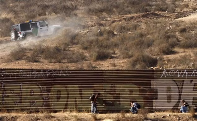 Những người di cư ẩn nấp trốn chiếc xe tuần tra biên giới trong khi chờ cơ hội chạy sang Mỹ tại hàng rào biên giới ở vùng ngoại ô Tijuana ngày 19/9/2009.