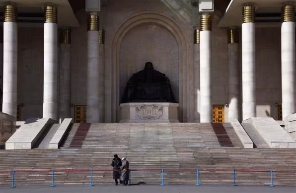 Một người đàn ông mặc trang phục truyền thống của Mông Cổ đứng nói chuyện với nhân viên bảo vệ phía trước bức tượng Thành Cát Tư Hãn của tòa nhà Quốc hội tại Ulaanbaatar ngày 3/4/2012.