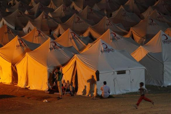 Một người tị nạn Syria cầu nguyện trong khi gia đình anh đang ngồi phía trước lều của họ tại một trại tị nạn ở Yayladagi, tỉnh Hatay ngày 19/6/2011.